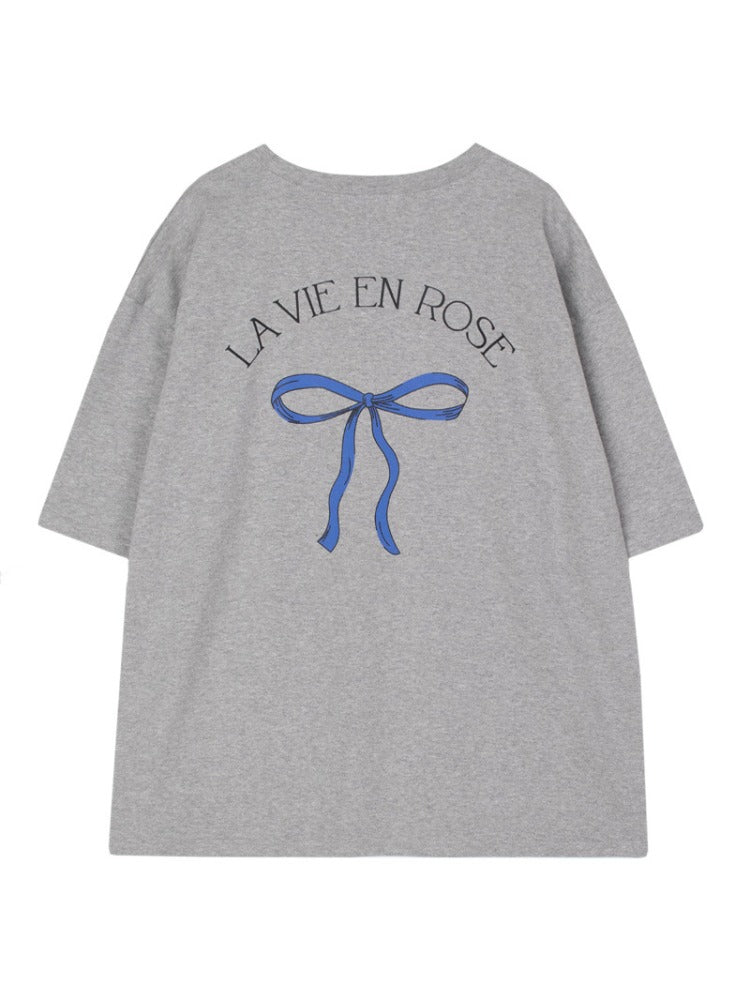 Graues T-Shirt mit blauem Schleifenmotiv und "La Vie en Rose"-Aufdruck. Modisches Damenoberteil, lässiger Stil, hochwertiger Baumwollstoff.