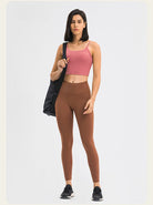 Frau in sportlicher Kleidung: rosa Sport-BH, braune Leggings, schwarze Sneakers. Fitnessmode, Sportbekleidung, aktiver Lebensstil.
