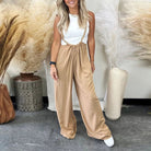 Frau in eleganter, beiger Latzhose und weißem Top, umgeben von dekorativen Pampasgras-Vasen. Modetrend, lässiger Stil, Damenbekleidung.