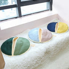 Runde Sitzkissen in Grün, Blau und Gelb auf weißem Fellteppich. Perfekt für modernes Wohndesign, gemütliche Dekoration und Komfort.