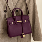 Lila Lederhandtasche mit goldener Hardware, elegant, auf braunem Mantel hängend.