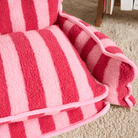 Gestreiftes Katzenbett aus Lammwolle in Rosa und Rot auf Teppichboden.