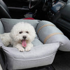 Weißer Hund in grauem orthopädischen Autositz für Haustiere, sicherer Hundesitz im Auto.