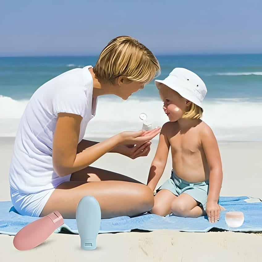 Frau und Kind am Strand mit Sonnencreme, blaues Handtuch, Sommer, Hautschutz, Meer im Hintergrund.