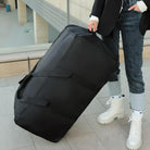 Person mit großer schwarzer Reisetasche, Jeans und weißen Stiefeln auf einem Gehweg.
