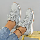 Silberne Glitzer-Sneaker auf gelbem Stuhl, kombiniert mit zerrissenen Jeans. Modische Damen-Schuhe, ideal für trendige Freizeit-Looks.