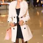 Eleganter Damenmantel mit weißem Kunstpelzkragen, doppelt geknöpft, ideal für Wintermode. Perfekt kombiniert mit schwarzem Kleid und rosa Tasche.