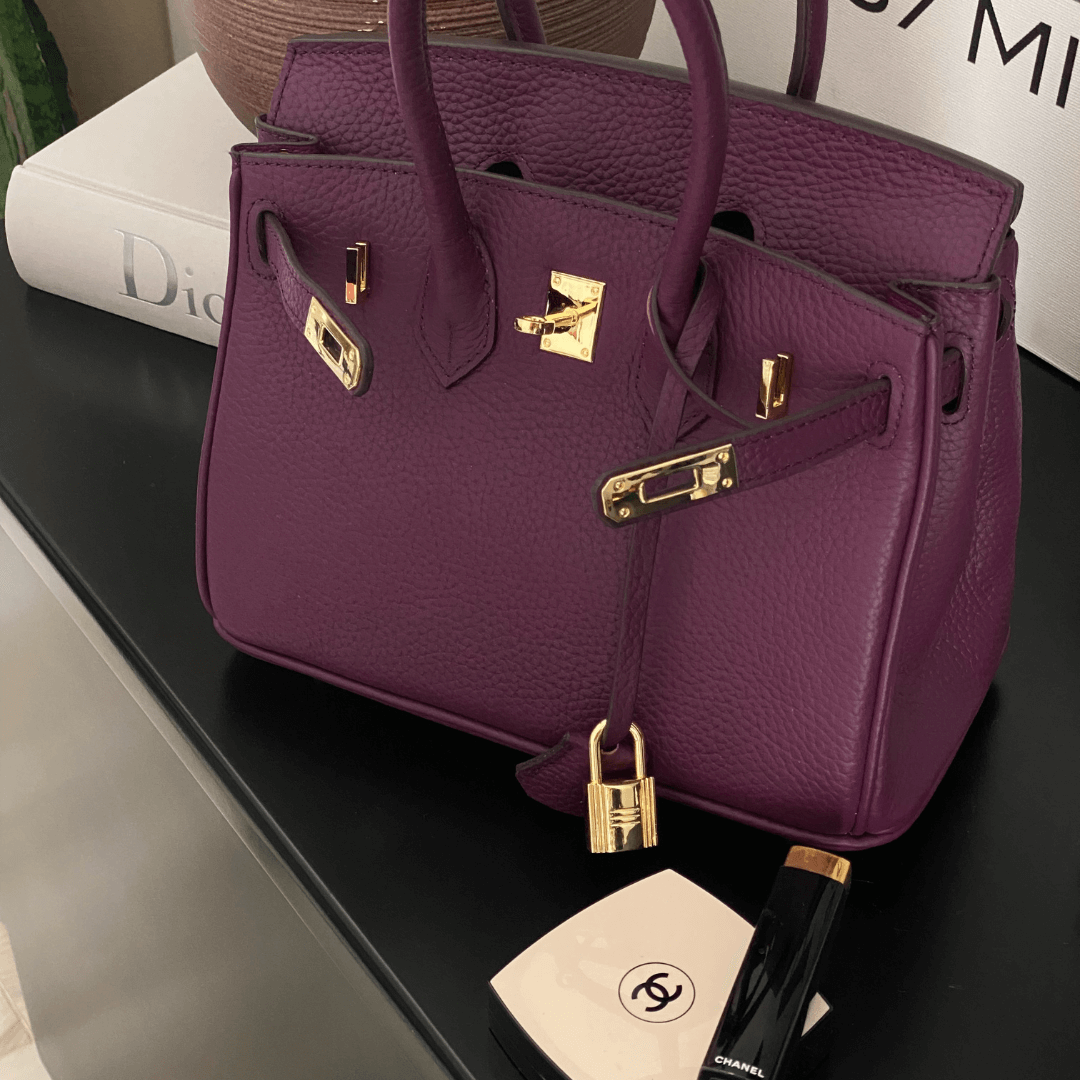 Lila Designer-Handtasche aus Leder mit goldenen Beschlägen auf schwarzem Tisch, Chanel Make-up.