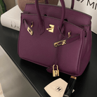 Lila Designer-Handtasche aus Leder mit goldenen Beschlägen auf schwarzem Tisch, Chanel Make-up.