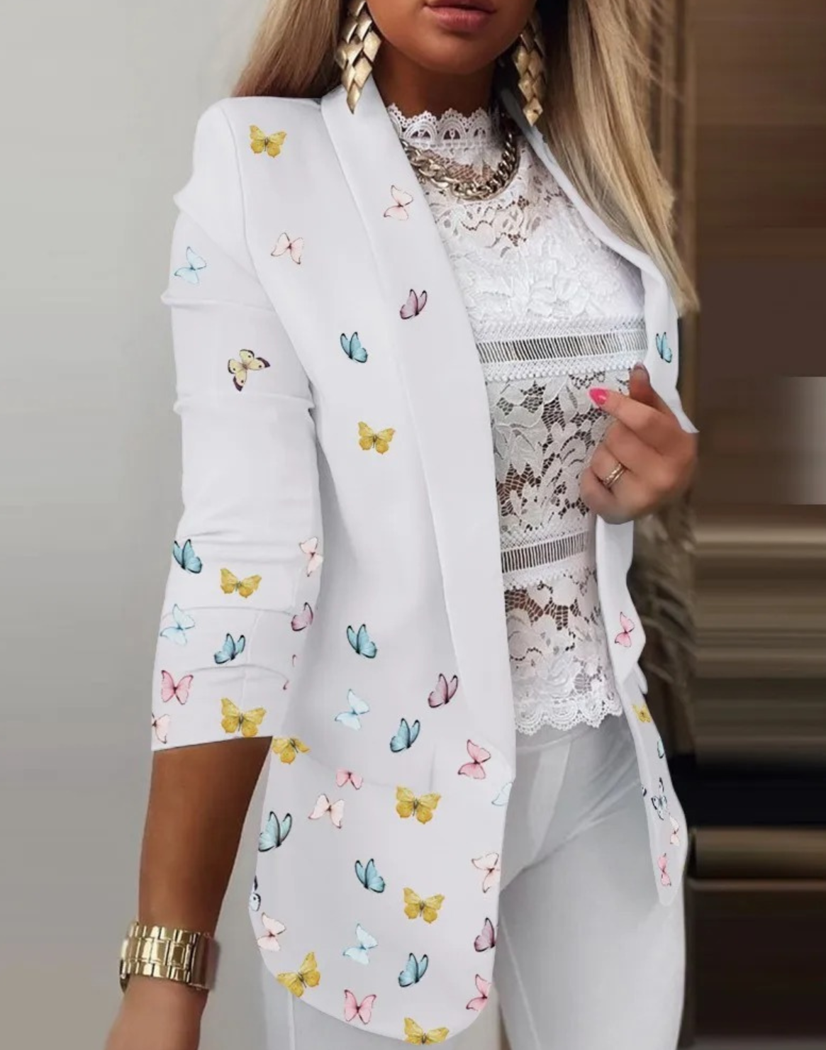 Eleganter weißer Blazer mit buntem Schmetterlingsmuster, kombiniert mit Spitzenbluse und goldenen Accessoires. Perfekt für modische Damenoutfits.