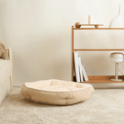 Beiges Cord-Samt-Haustierbett, rund, flauschig, auf Teppich vor Regal im Wohnzimmer.