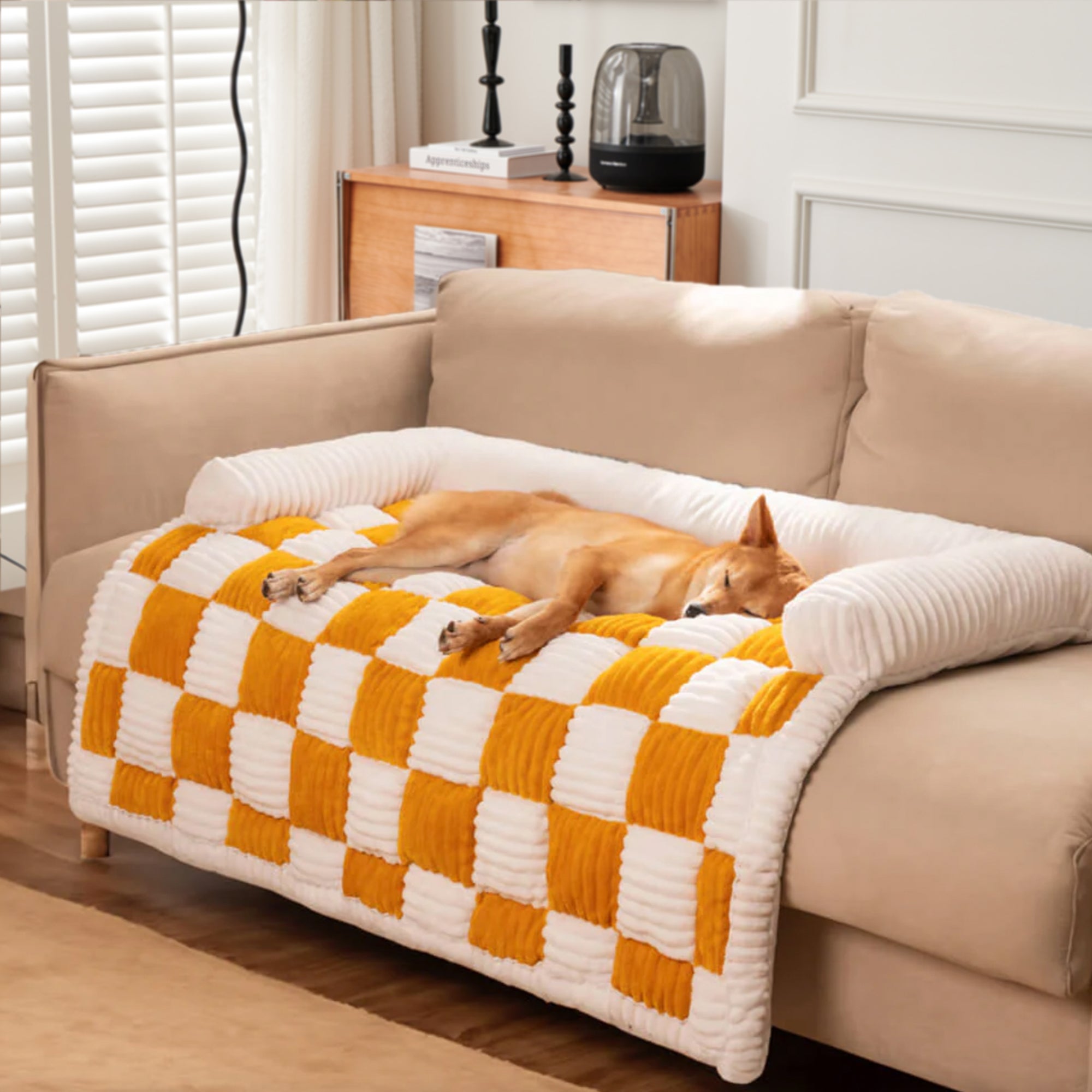 Beige-orange kariertes Hundebett auf Sofa, gemütlicher Möbelbezug, quadratisches Design.