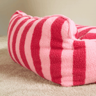 Rosa-rot gestreiftes Katzenbett aus Lammwolle auf Teppich, gemütlich und stilvoll.