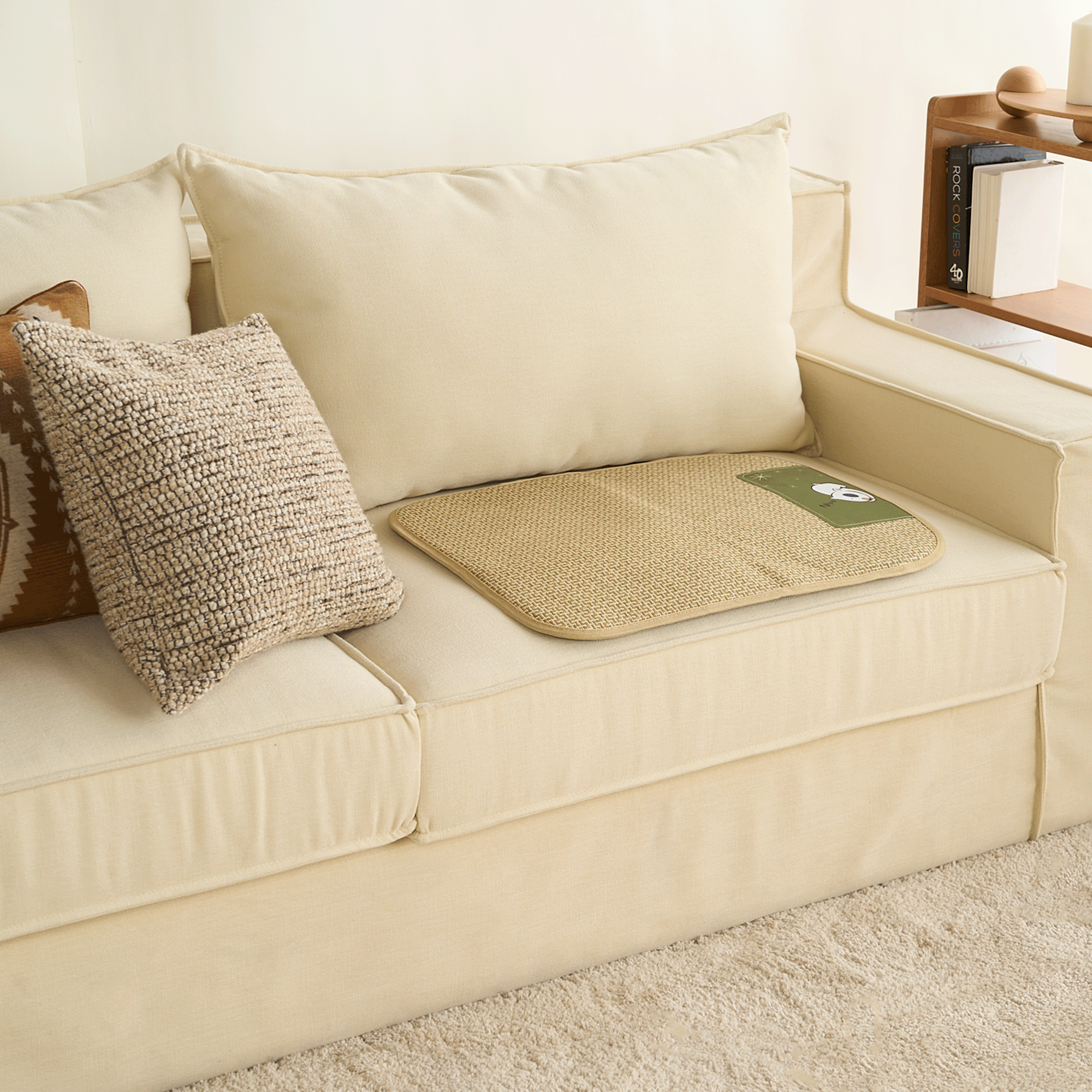 Geflochtete Rattan-Kühlmatte für Haustiere auf beigem Sofa, umgeben von Kissen.