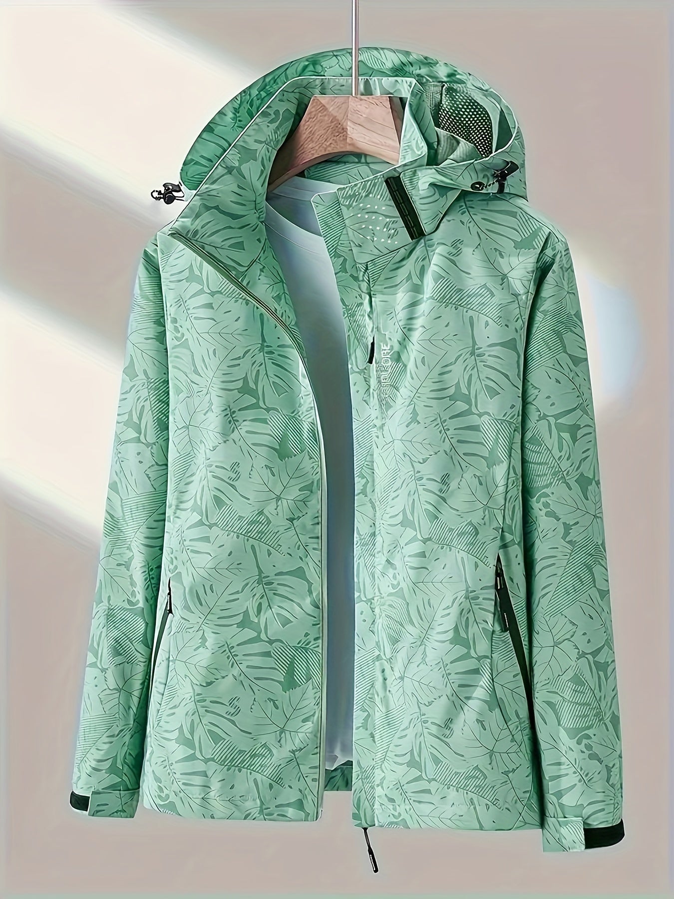 Grüne Outdoor-Jacke mit Blattmuster, wasserdicht und atmungsaktiv, ideal für Wandern und Trekking. Funktionale Kapuze und Reißverschlüsse.