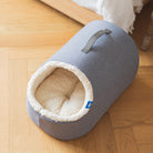 Graues Katzenbett aus Stoff mit weichem Innenfutter auf Holzboden.