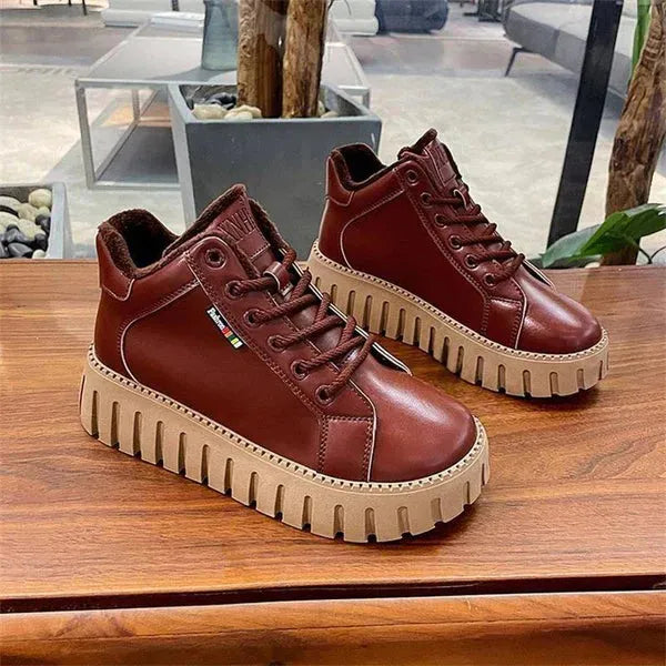 Braune Leder-Sneaker mit dicker, geriffelter Sohle auf Holztisch. Modische, bequeme Schuhe für Damen und Herren. Ideal für Freizeit und Alltag.
