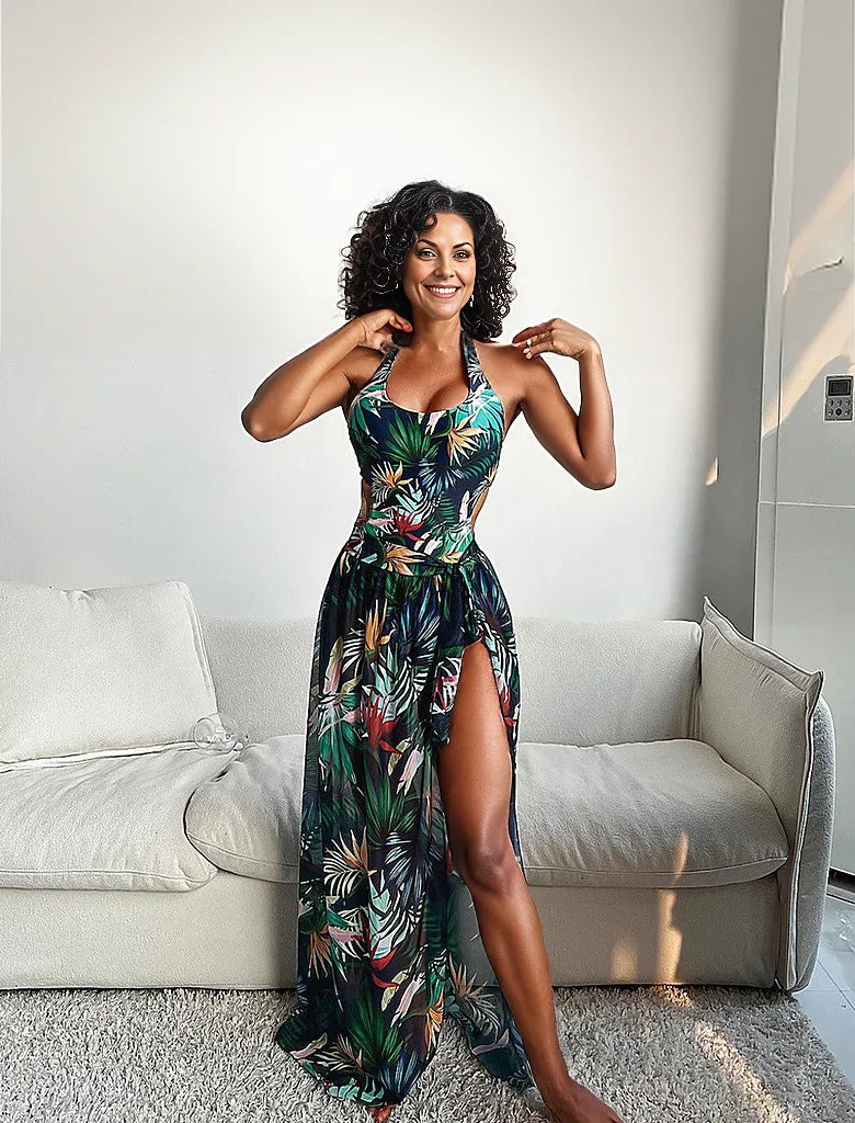 Frau in tropischem Maxikleid mit Blumenmuster, lächelnd im Wohnzimmer. Sommermode, elegantes Design, trendige Damenbekleidung.