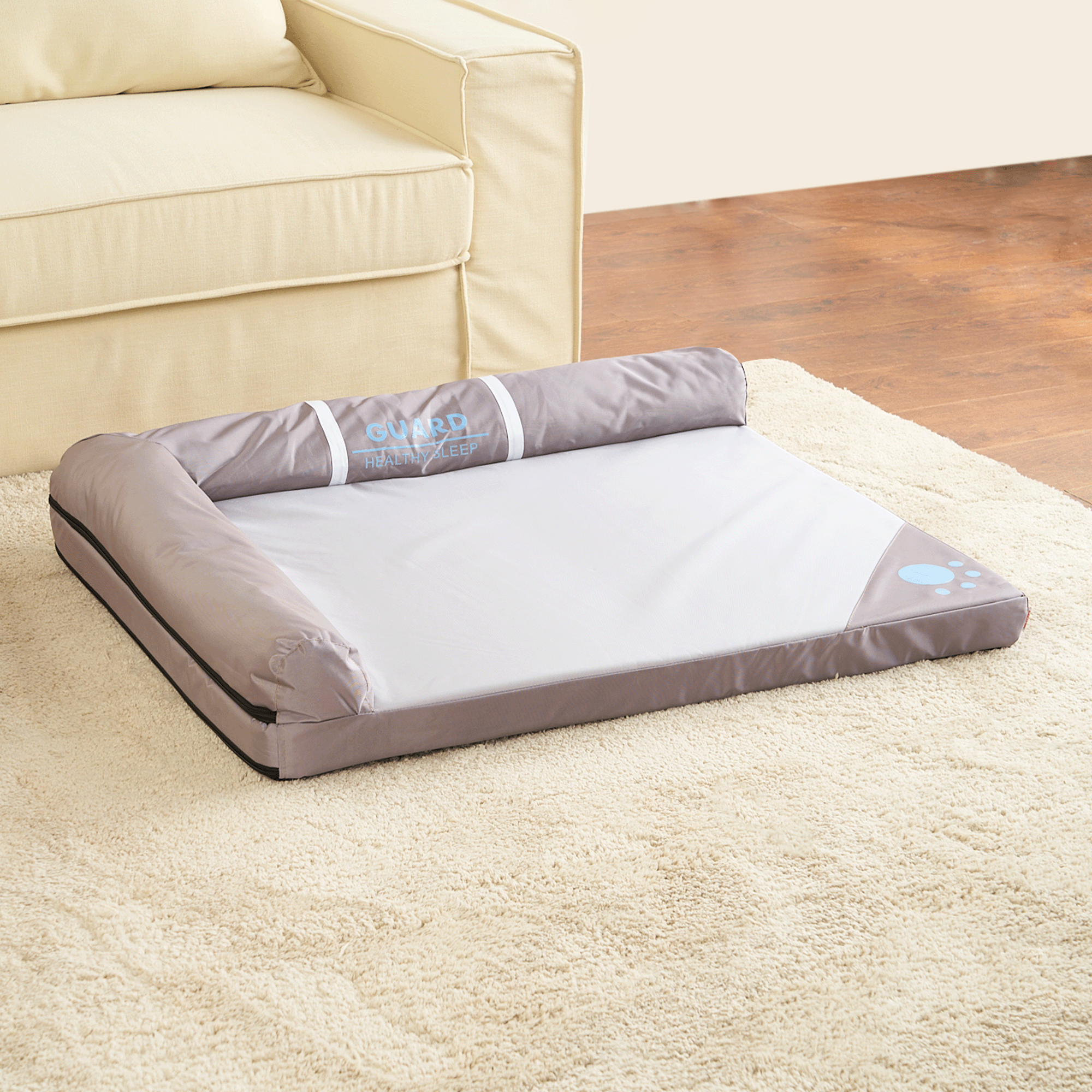 Graues modernes Haustierbett auf beigem Teppich neben beigem Sofa, ideal für Hunde und Katzen.