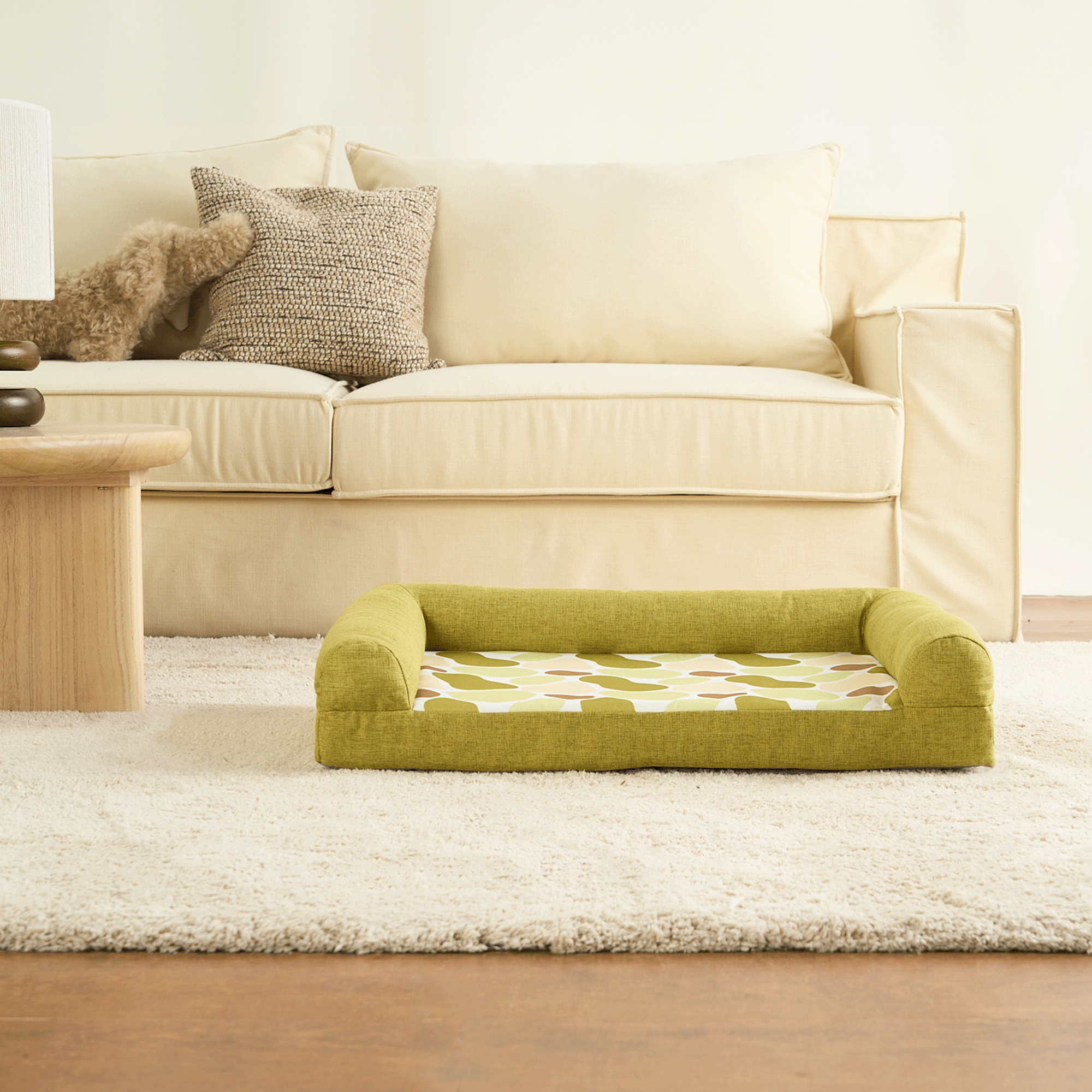 Grünes Haustierbett mit abnehmbarem Bezug vor beiger Couch auf Teppich.