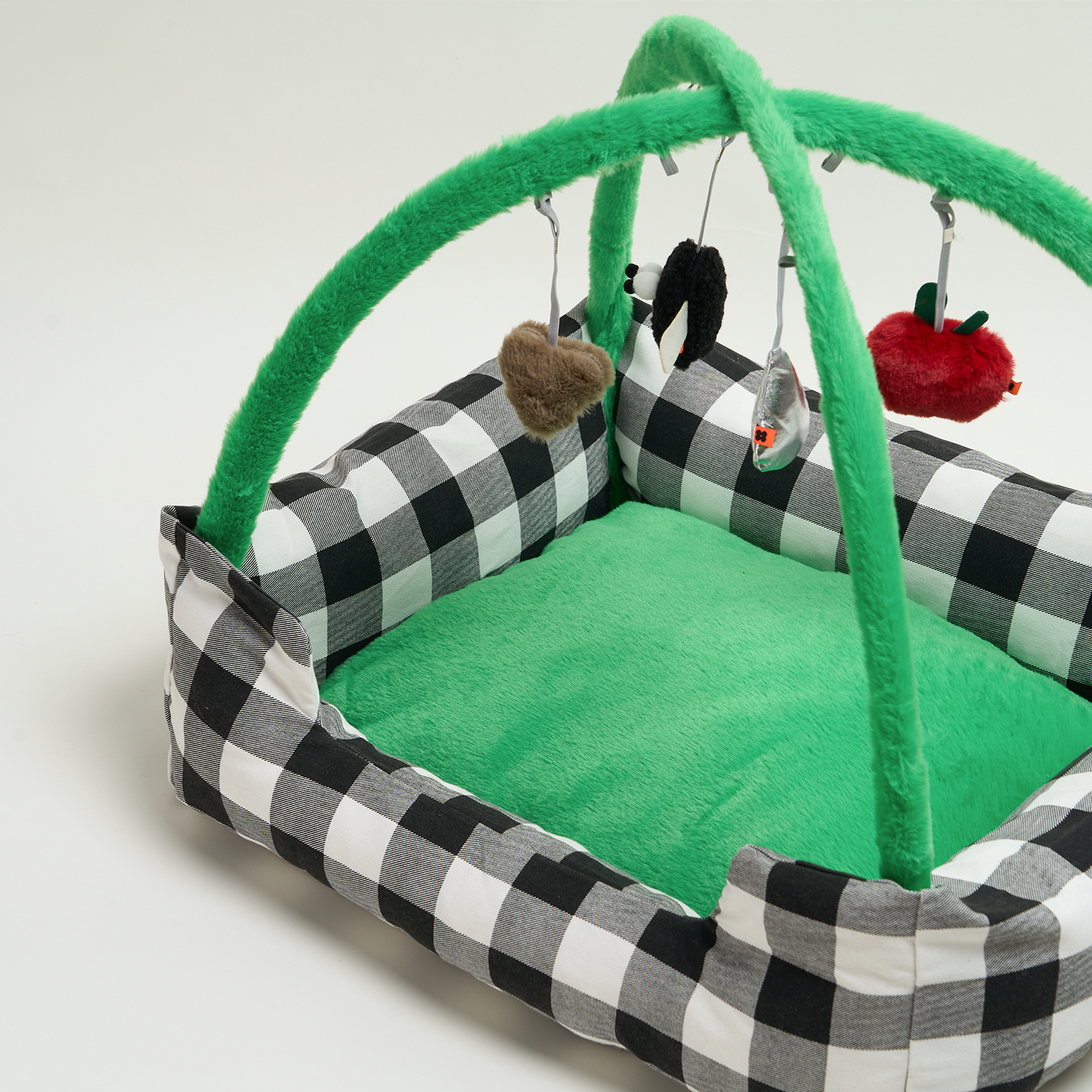 Schwarz-weiß kariertes Katzenbett mit grünem Plüschboden und hängendem Spielzeug.