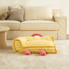 Gelbes Haustierbett in Kükenform auf Teppich vor beigem Sofa, gemütliches Design.
