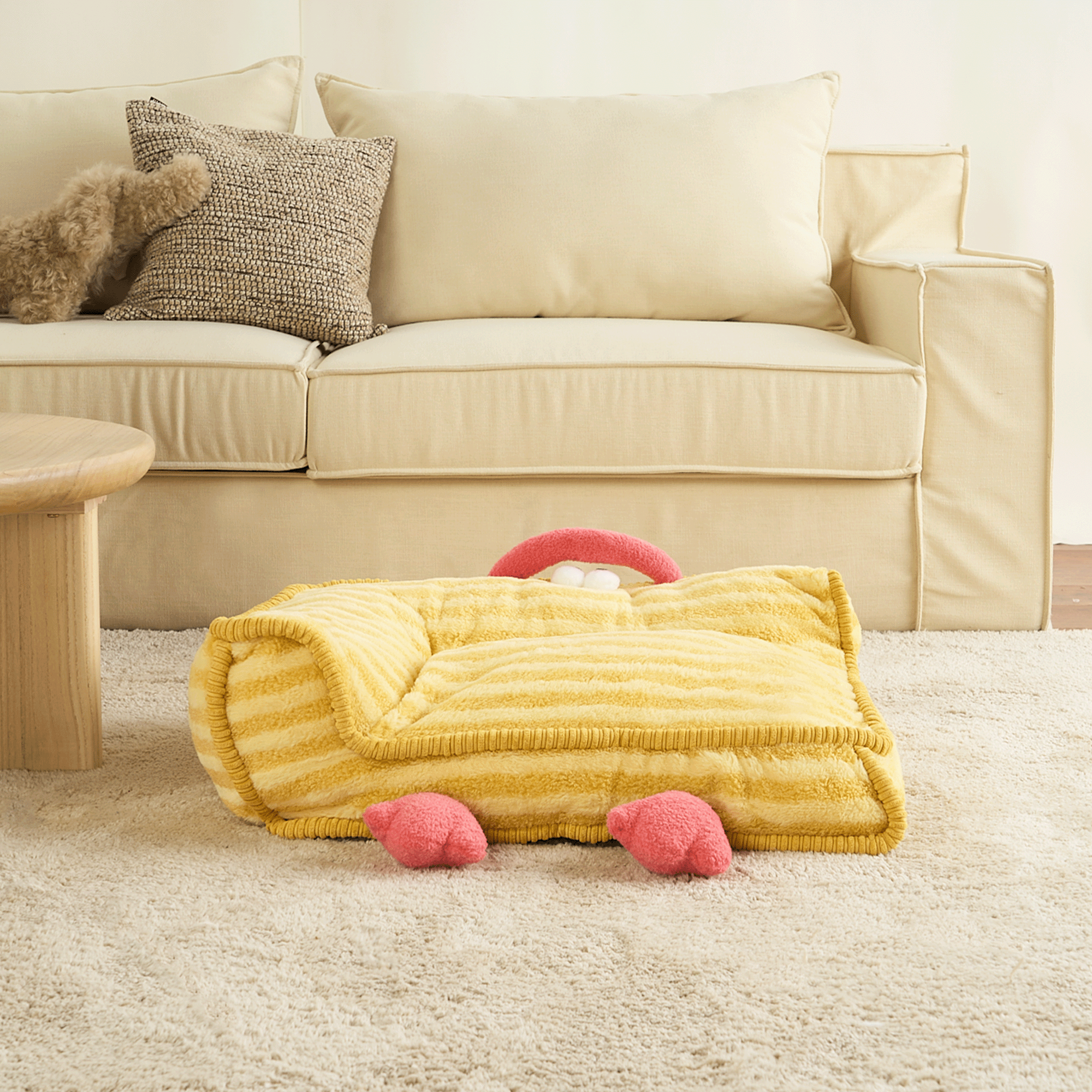 Gelbes Haustierbett in Kükenform auf Teppich vor beigem Sofa, gemütliches Design.