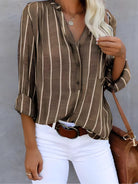 Damenbluse mit braun-weißen Streifen, lässig geschnitten, kombiniert mit weißer Hose und brauner Tasche. Perfekt für modische Freizeitlooks.