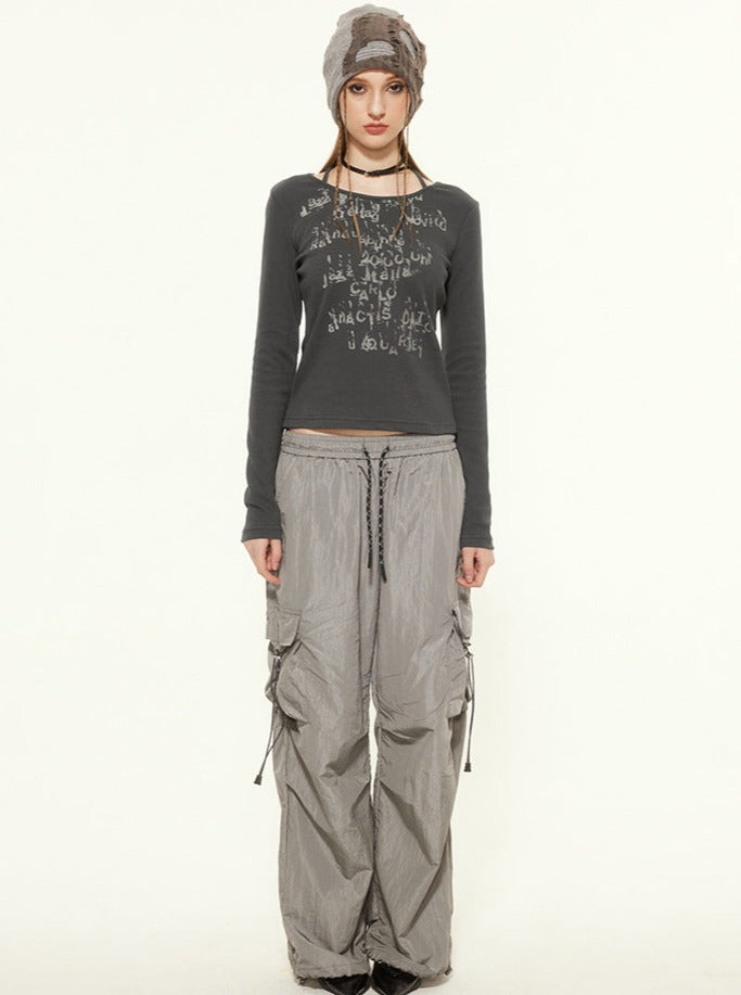 Frau in grauem Langarmshirt mit Schriftzug, weiten Cargo-Hosen und Mütze. Modetrend, urbaner Stil, lässige Damenbekleidung.