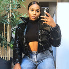 Frau in glänzender schwarzer Daunenjacke, schwarzem Crop-Top und Jeans, macht Selfie. Modetrend, Winterjacke, Streetstyle, Damenmode.