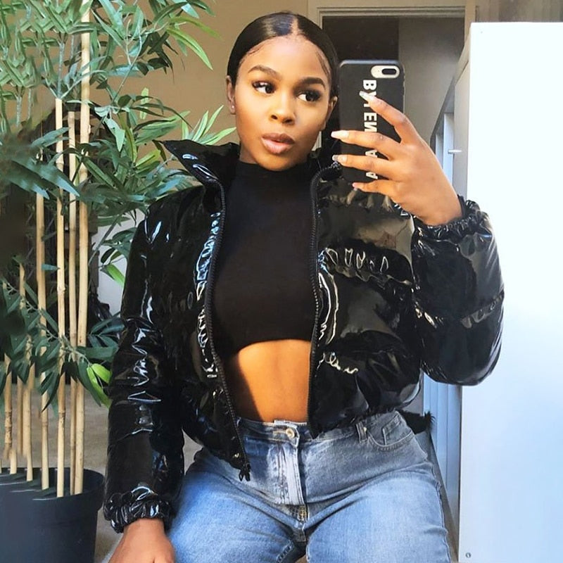 Frau in glänzender schwarzer Daunenjacke, schwarzem Crop-Top und Jeans, macht Selfie. Modetrend, Winterjacke, Streetstyle, Damenmode.
