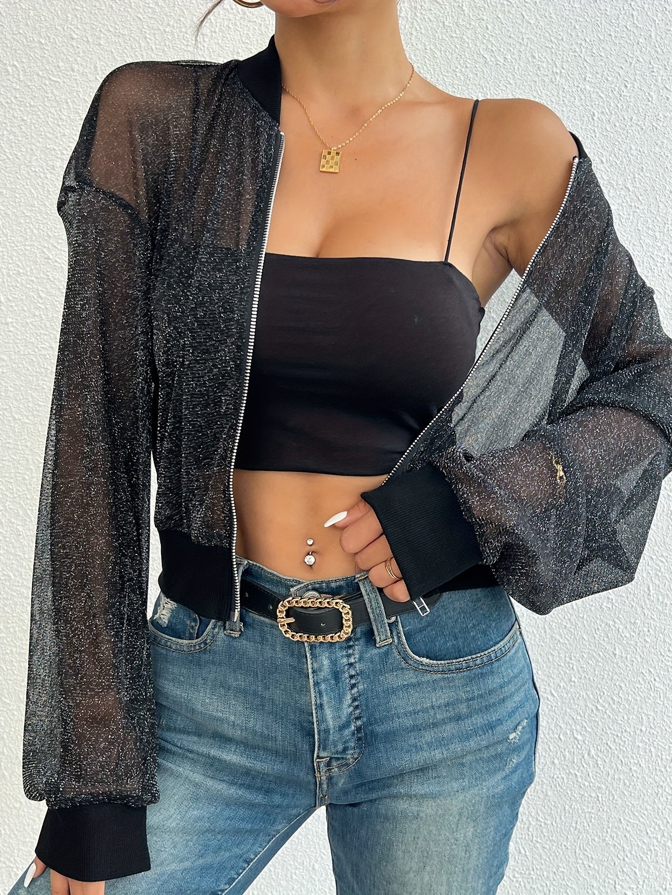 Funkelnde schwarze Netzjacke über schwarzem Top, kombiniert mit blauer Jeans. Modetrend, Damenmode, stilvolle Outfits, lässiger Chic.