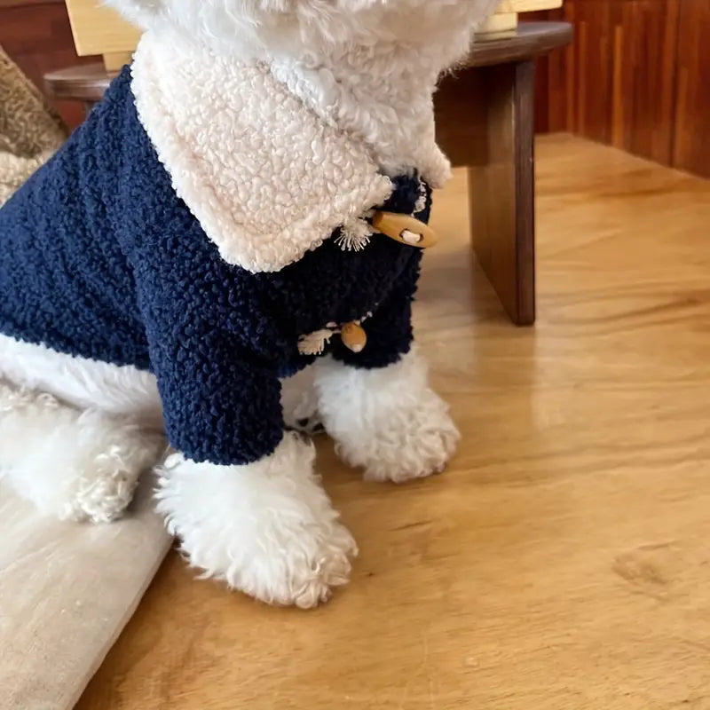 Weißer Hund in blauem, flauschigem Mantel mit Holzknöpfen auf Holzboden. Stilvolle Hundebekleidung, warmes Haustieroutfit, modischer Hundemantel.