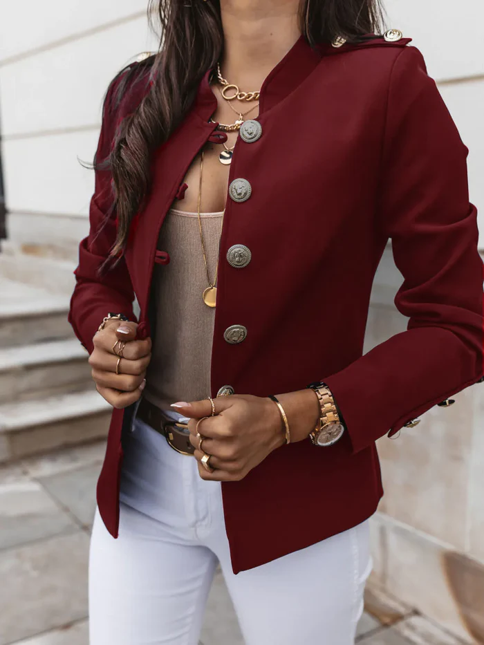 Damenblazer in Bordeauxrot mit goldenen Knöpfen, kombiniert mit weißer Hose und Schmuck. Elegante Mode, stilvoller Look, Herbsttrends.