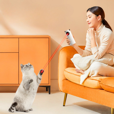 Frau spielt mit Katze und Laserpointer im Wohnzimmer. Moderne Einrichtung, orangefarbenes Sofa, interaktives Katzenspielzeug, Haustierunterhaltung.