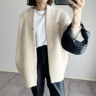Damenmode: Eleganter, cremefarbener Cardigan über weißem T-Shirt, kombiniert mit schwarzer Hose und geflochtener Handtasche. Trendiger Herbstlook.