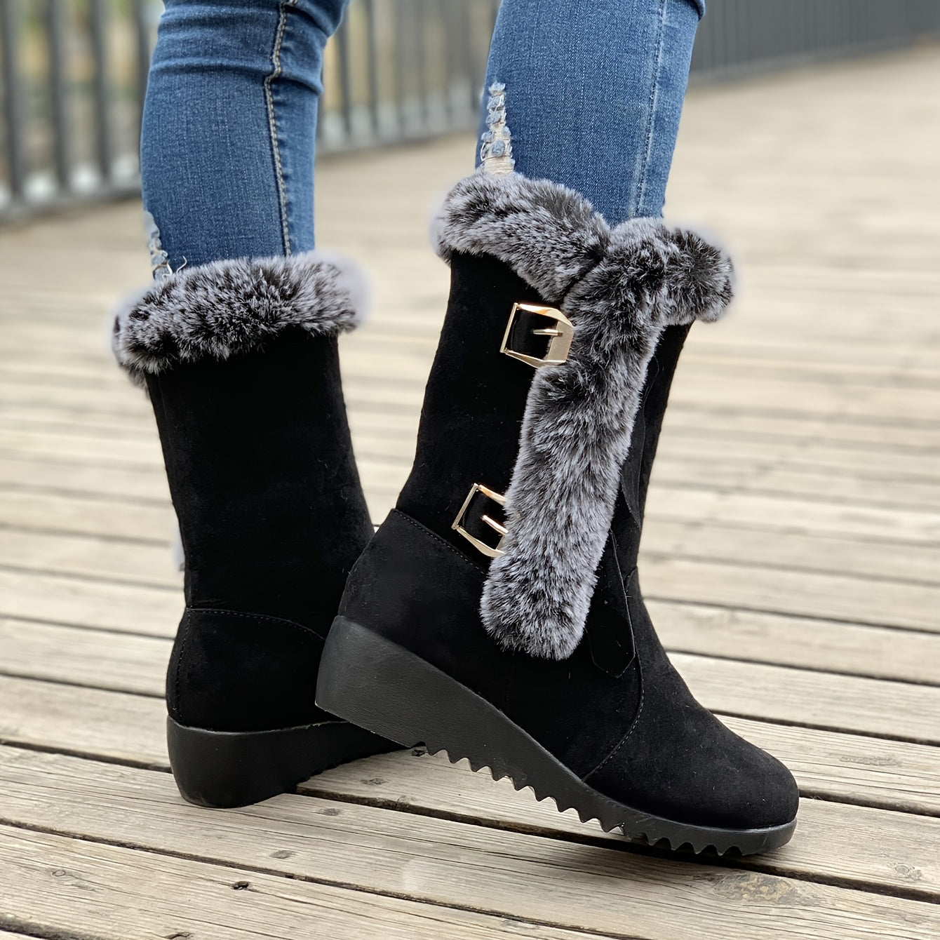 Schwarze Winterstiefel mit Kunstfellbesatz und Schnallen, getragen auf Holzsteg. Modische Damenstiefel, warm und stilvoll für kalte Tage.