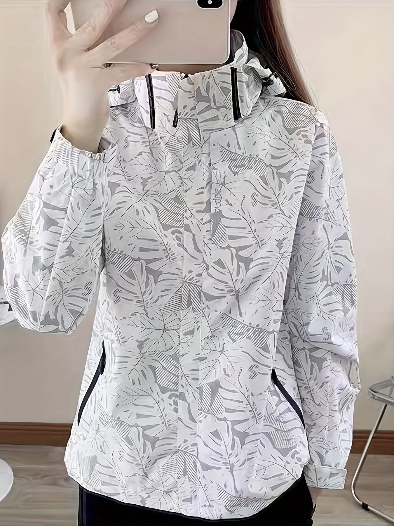 Weiße Damenjacke mit tropischem Blattmuster, Kapuze und Reißverschlusstaschen. Modische Outdoor-Bekleidung, ideal für Frühling und Herbst.