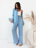 Frau in hellblauem Leinenanzug mit weißem Top, hält eine blaue Clutch. Modetrend, Sommeroutfit, lässiger Stil, Damenmode, Leinenkleidung.