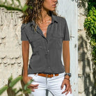 Frau in grauer Bluse und weißer Hose vor Steinwand, Sommermode, Freizeitkleidung.