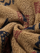 Beigefarbener Fleece-Stoff mit blau-rotem Muster, weiche Textur, ideal für warme Kleidung.