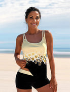 Frau in gelbem Tankini mit Blumenmuster am Strand, lächelnd. Sommermode, Bademode, Strandoutfit, Damenbekleidung, stilvoller Look.