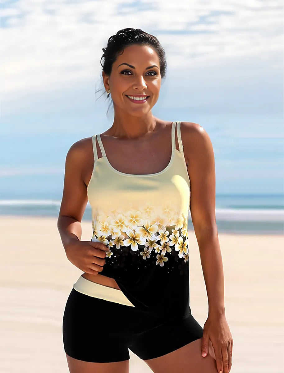 Frau in gelbem Tankini mit Blumenmuster am Strand, lächelnd. Sommermode, Bademode, Strandoutfit, Damenbekleidung, stilvoller Look.