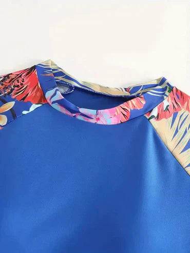 Blaues Damenoberteil mit tropischem Blumenmuster an den Ärmeln, ideal für Sommermode. Perfekt für Strand- und Freizeitoutfits.