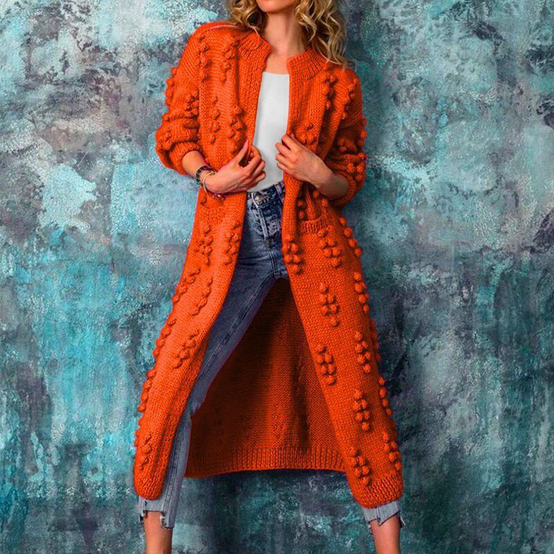 Langer, orange Strickmantel mit auffälligem Noppenmuster, kombiniert mit weißem Top und Jeans. Modetrend, Herbstmode, Damenbekleidung.