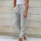 Frau in grauer Leinenhose und weißem Top vor Holzwand, lässige Sommermode.