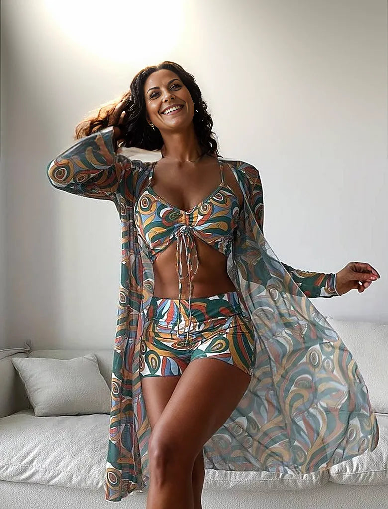 Frau in gemustertem Strandoutfit mit Kimono, Bikini-Top und Shorts. Sommermode, Boho-Stil, farbenfrohes Design, ideal für Strandurlaub.