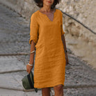 Frau in senfgelbem Leinenkleid, lässig und stilvoll, auf Kopfsteinpflaster. Perfekt für Sommermode, Freizeitkleidung, Damenmode.