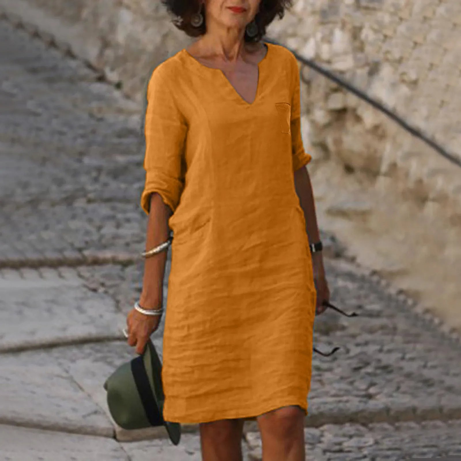 Frau in senfgelbem Leinenkleid, lässig und stilvoll, auf Kopfsteinpflaster. Perfekt für Sommermode, Freizeitkleidung, Damenmode.
