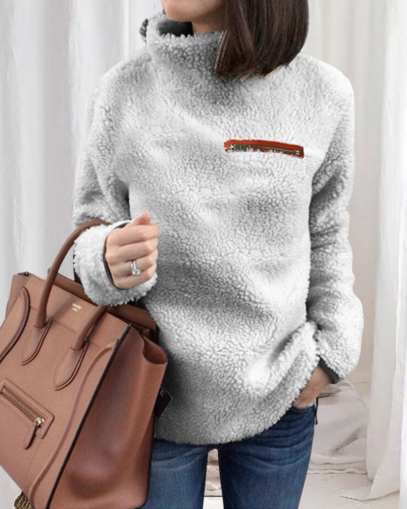 Damen Teddy-Fleece-Pullover in Grau mit hohem Kragen und Reißverschluss-Detail, kombiniert mit brauner Lederhandtasche. Wintermode, kuschelig, stilvoll.